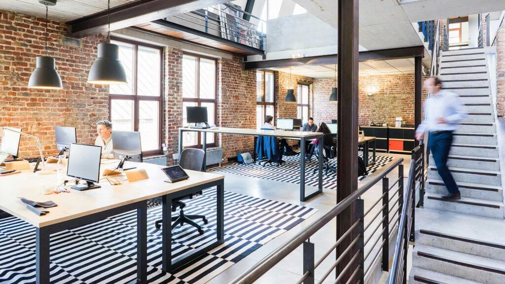 busy office with brick walls desks with people working custom lighting stairs and vaulted cieling
